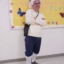 Ted in colonial dress with a white cap, cream shirt, breeches, and stockings
